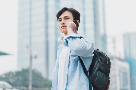 young asian man wearing a backpack and is on the phoneの写真素材
