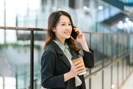 Portrait of a young Asian female director standing, drinking coffee and listening to the phoneの写真素材