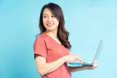Beautiful Asian woman using laptop on blue backgroundの写真素材
