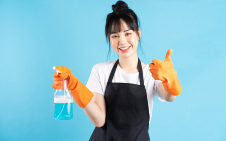 Asian housewife is wearing orange gloves and holding a spray of water in her handの写真素材