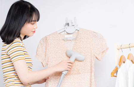 Beautiful Asian woman flattening her dress with the steam ironの写真素材