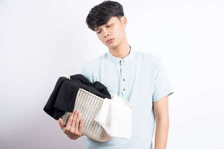 Young Asian man holding basket of clothes with gestures on white background