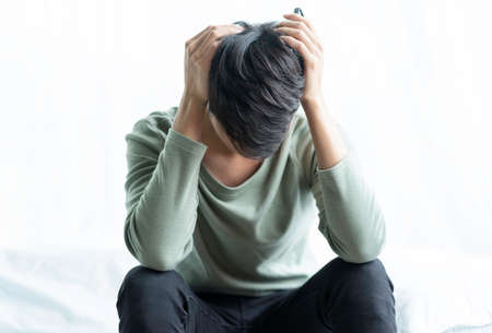 Portrait of young man sitting on a bed with his head tiredの写真素材
