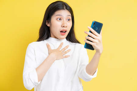 Young asian girl holding phone with expression on yellow backgroundの写真素材