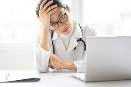 Portrait of young asian female doctor sitting on the desk with tired expression