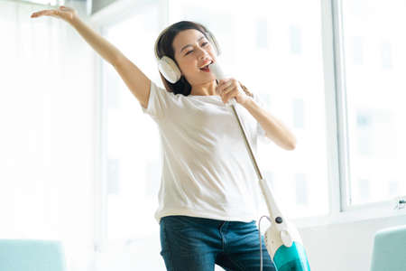 Asian woman listening to music and dancing with a vacuum cleanerの写真素材
