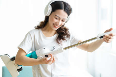 Asian woman listening to music and dancing with a vacuum cleanerの写真素材