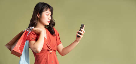 Asian woman is carrying shopping bag and staring at her phone