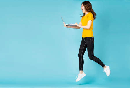 Young asian girl jumping up and using laptop on background