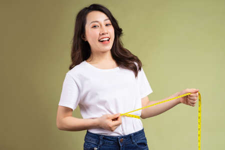 Young asian girl happily holding the tape measure after losing weightの写真素材
