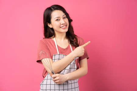 Housewife holding whisk cheerful expressive over pink backgroundの写真素材