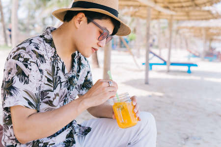 Young Asian man drinking orange juice on the beachの写真素材