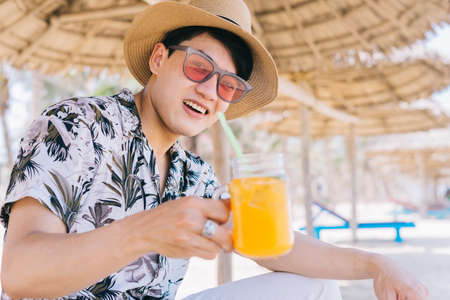 Young Asian man drinking orange juice on the beachの写真素材