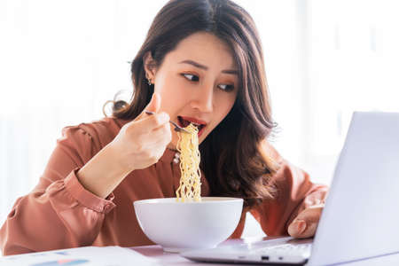 Asian businesswoman has to eat noodles while workingの写真素材