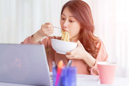 Asian businesswoman has to eat noodles while working