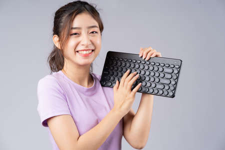 Young Asian girl using keyboard on grey background