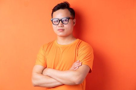 Asian man with arms crossed on orange backgroundの写真素材