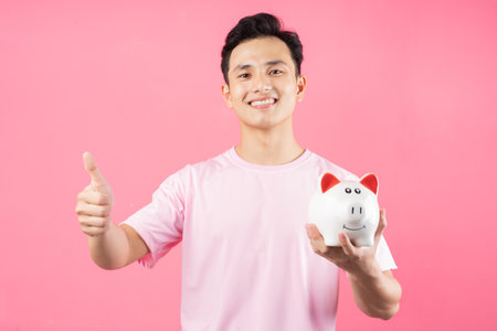 Young Asian man holding piggy bank on pink backgroundの写真素材