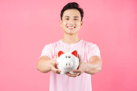 Young Asian man holding piggy bank on pink backgroundの写真素材