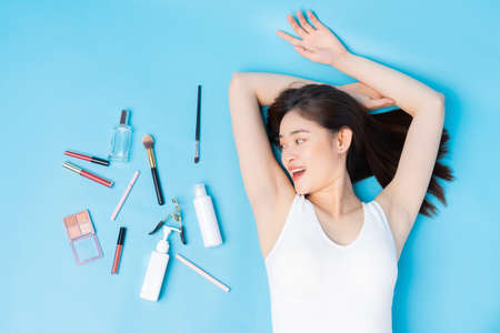 Woman lying on blue background with skin care tools and makeup besideの写真素材