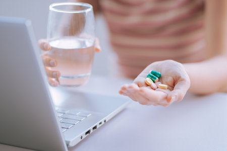 Young Asian woman holding cup of water and medicine in hand to prepare for useの写真素材