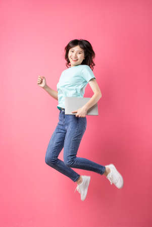 Young girl holding laptop jumping up on background