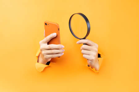 Hand holding magnifying glass and phone protruding from background