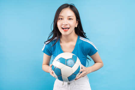 Beautiful Asian woman posing with soccer ball on blue backgroundの写真素材
