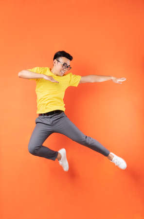 Asian man in yellow t-shirt jumping on orange backgroundの写真素材