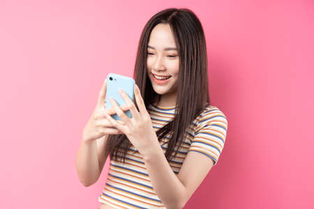 Young Asian woman using smartphone on pink background