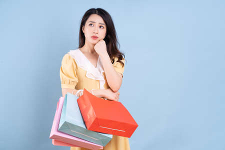 Beautiful young Asian woman holding shopping bag on blue background