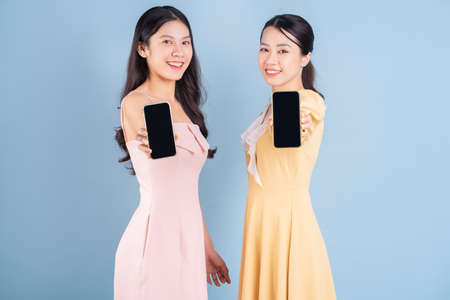 Two young Asian women wearing dress on blue background