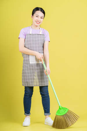 Young Asian housewife posing on yellow backgroundの写真素材