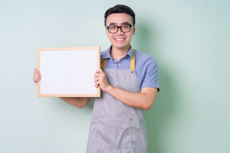 Young Asian man wearing apron posing on green backgroundの写真素材
