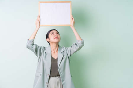 Young Asian businesswoman holding white board on green background