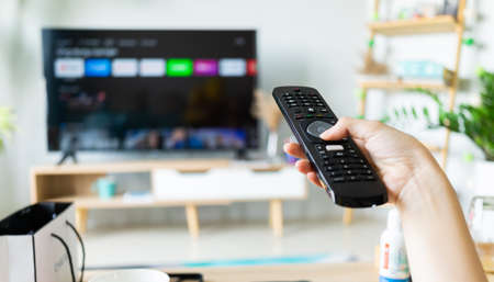 Asian woman holding tv remote in hand to change channelの写真素材
