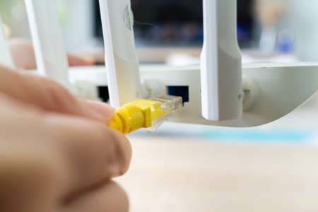 Asian woman plugging network cable into routerの写真素材