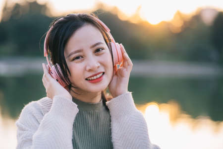 Beautiful Asian girl is listening to music by the lakeの写真素材