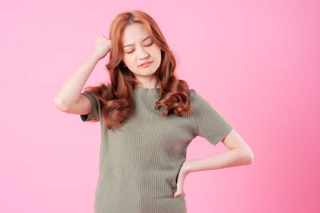 Young Asian woman sitting and using laptop on pink background