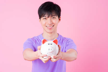 Young Asian man holding pink giftbox on pink background