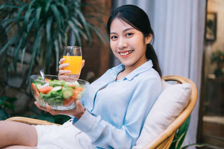 Beautiful young Asian woman enjoying breakfast with saladの写真素材