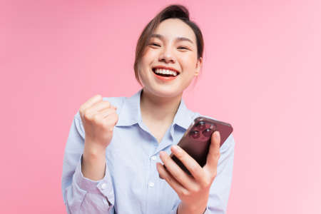 Image of young Asian girl holding smartphone on pink backgroundの写真素材