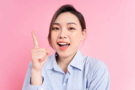 Image of young Asian business woman holding laptop on pink backgroundの写真素材