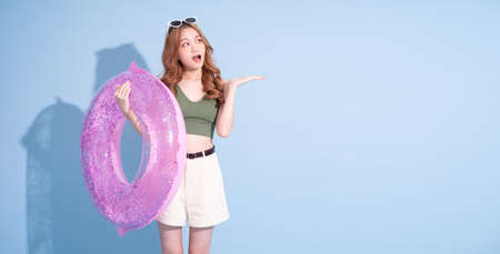 Image of young Asian girl holding swimming float on blue background, summer vacation concept