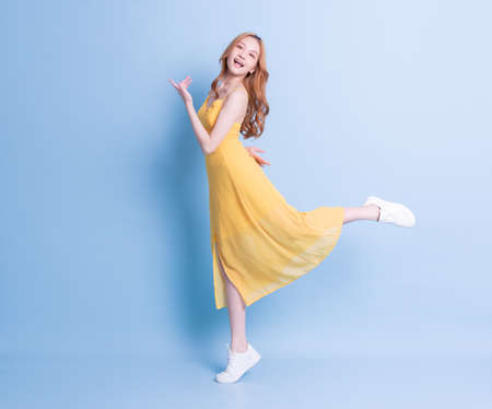 Full length image of young Asian woman wearing yellow dress on blue backgroundの写真素材