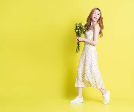 Image of young Asian woman holding flowers on yellow backgroundの写真素材