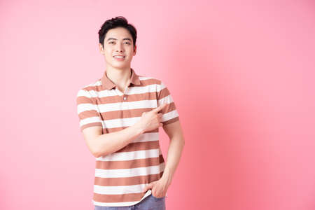 Portrait of young Asian man using laptop on pink backgroundの写真素材