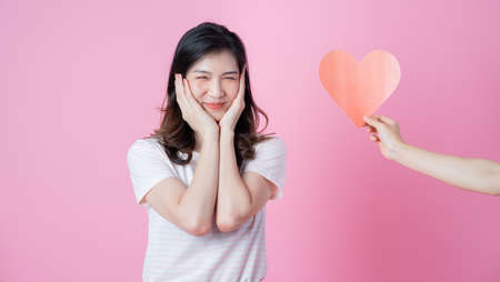 Young Asian girl holding heart shape on pink backgroundの写真素材