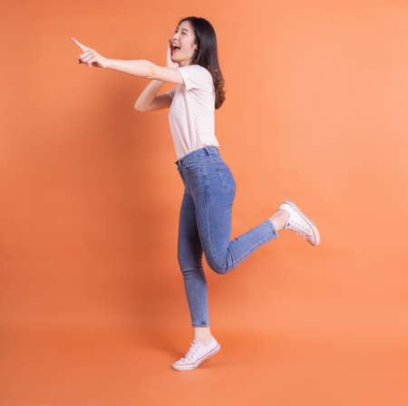 Full length image of young Asian woman posing on orange backgroundの写真素材