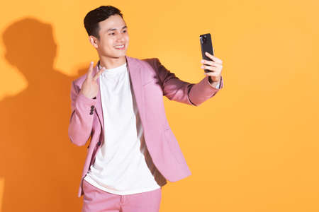 Full length image of young Asian man  standing on orange background